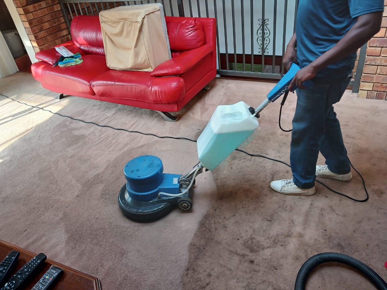 Estlas team using a rotary carpet cleaner beside a red sofa